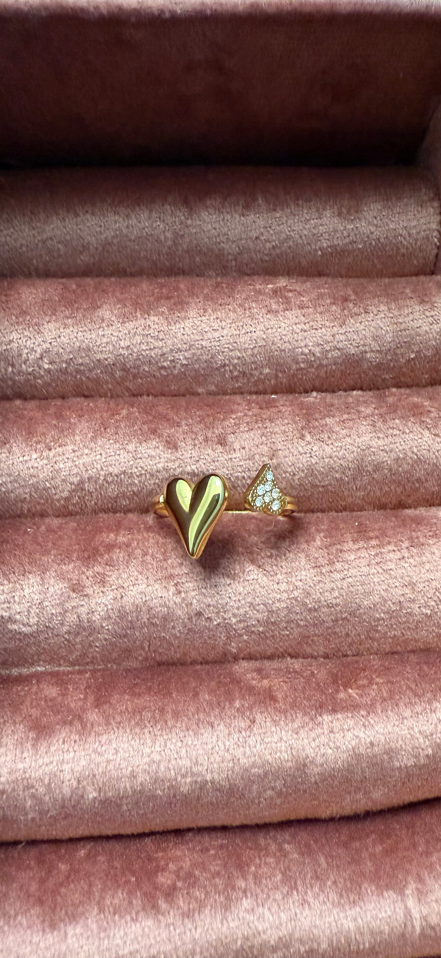 Goudkleurige open stainless steel ring met een glanzend hartje en subtiele zirkonia steentjes, gepresenteerd op roze fluweel