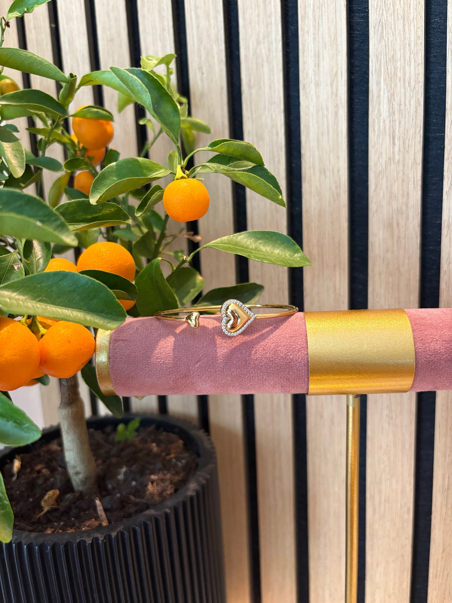 Heart to Handle armband goudkleurig – open bangle met hartvormige uiteinden, modern design gepresenteerd op roze display
