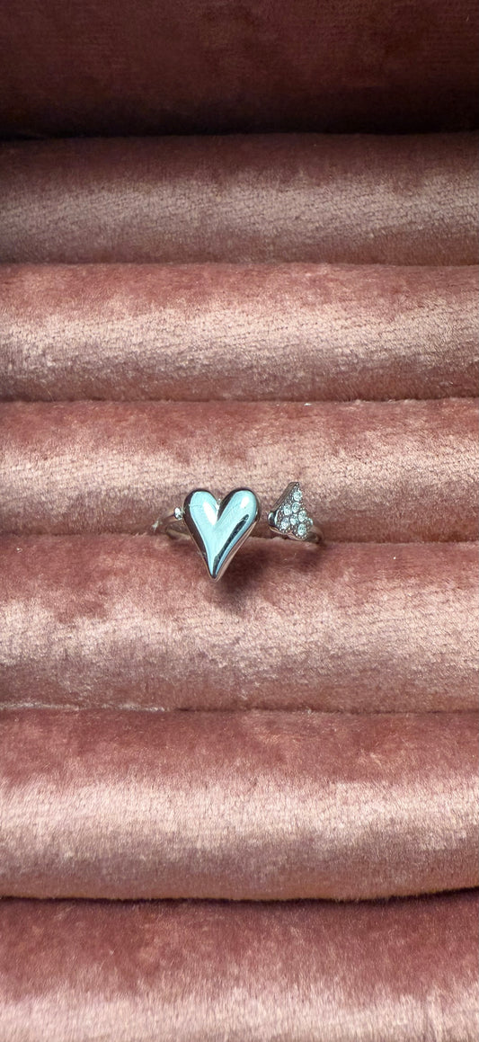 Zilverkleurige open stainless steel ring met een glanzend hartje en subtiele zirkonia steentjes, gepresenteerd op roze fluweel