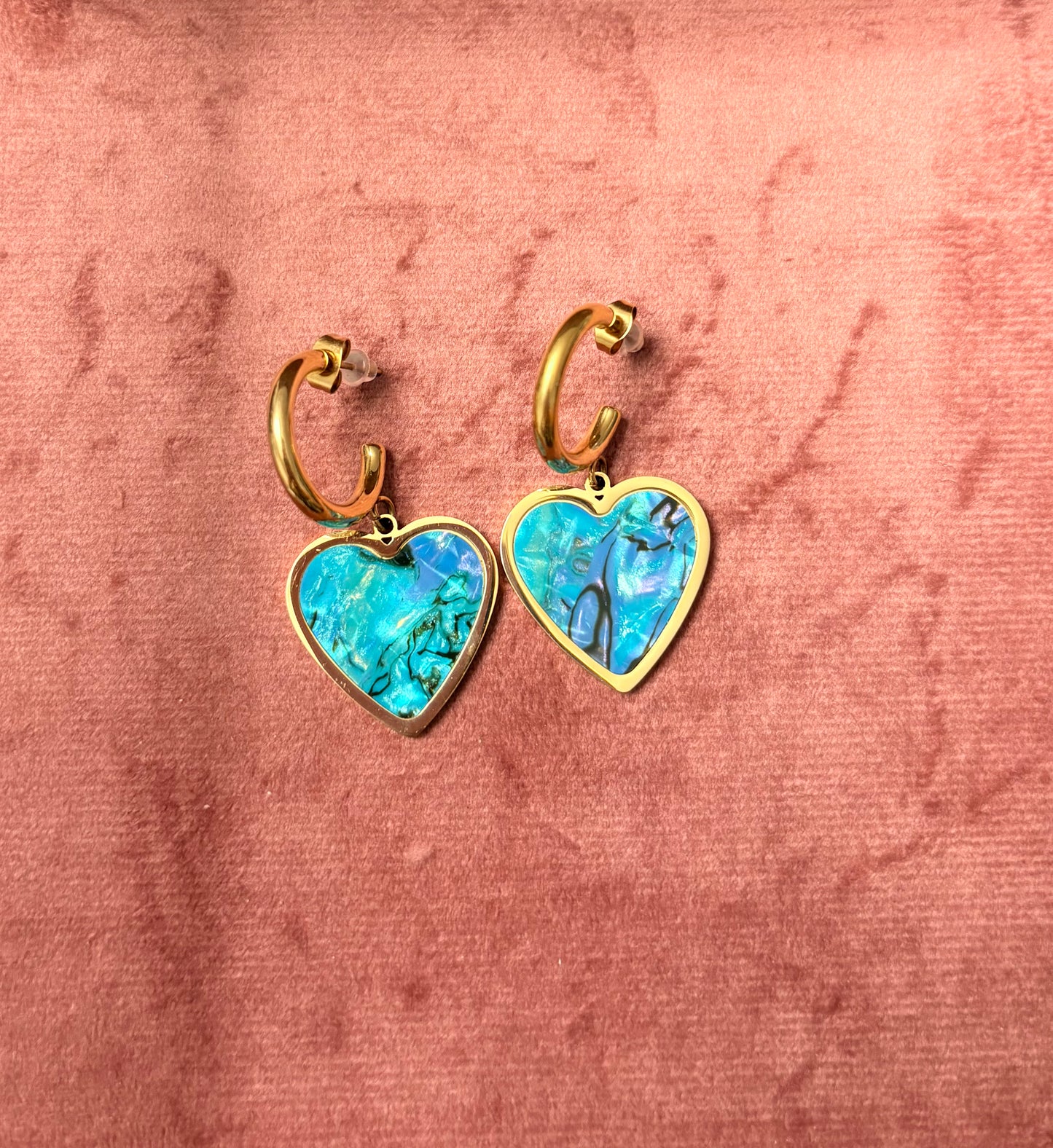 “Mood Swings” oorbellen – goudkleurige hoops met blauwe marmeren hartvormige bedels, gepresenteerd op een roze fluwelen achtergrond