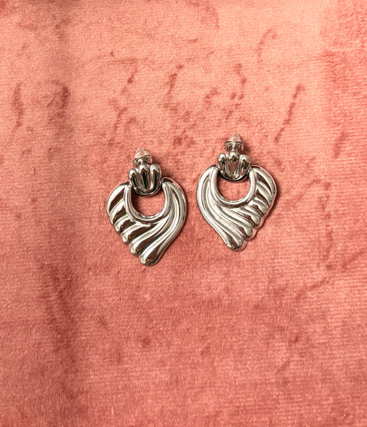 Zilverkleurige, abstract gevormde oorbellen met golvend reliëf, liggend op een roze fluwelen achtergrond