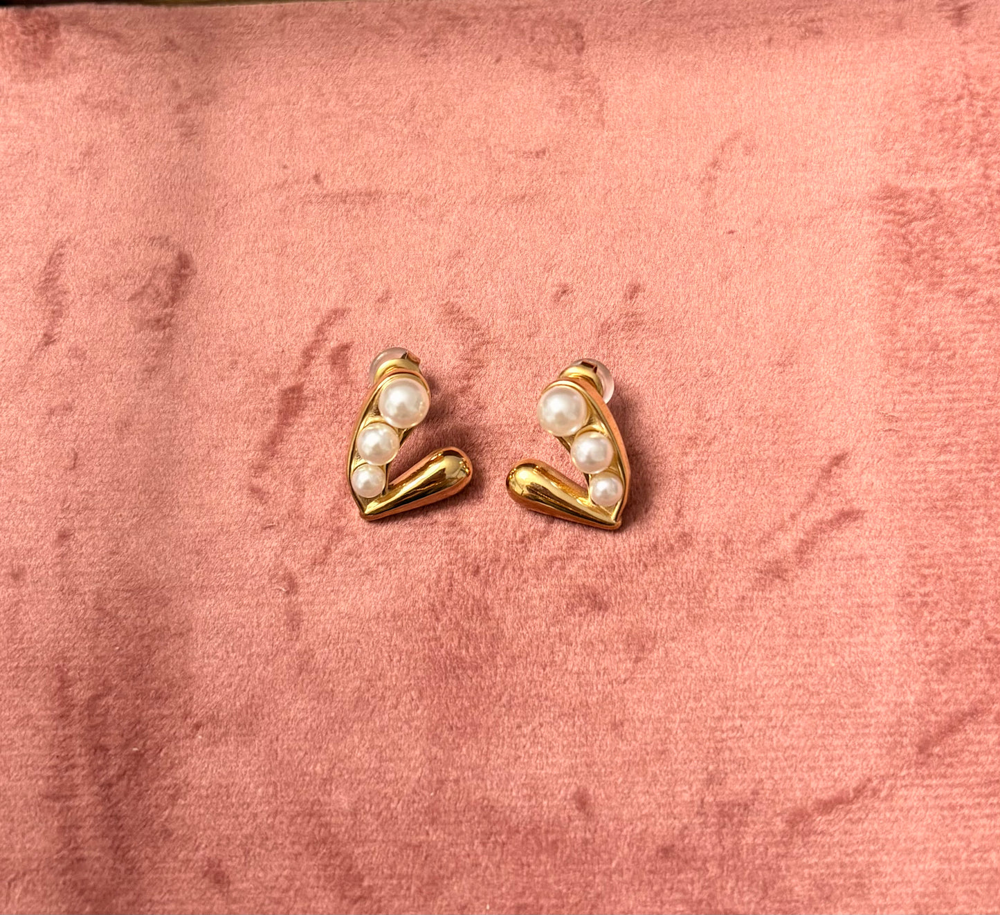 "Pearlfect Vibes" oorbellen – goudkleurige oorstekers met een V-design en meerdere witte parels, gefotografeerd op een roze fluwelen achtergrond