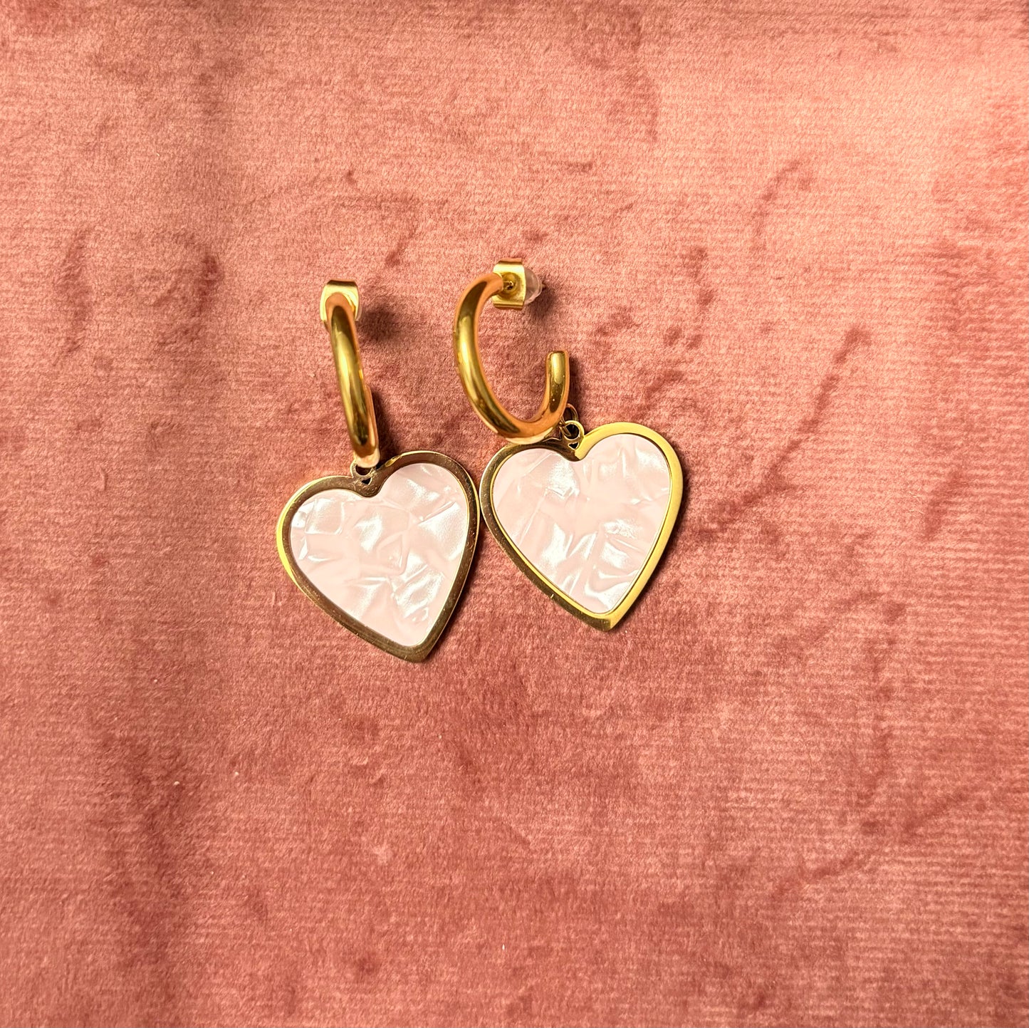 “Mood Swings” oorbellen – goudkleurige hoops met roze marmeren hartvormige bedel, gepresenteerd op een roze fluwelen achtergrond
