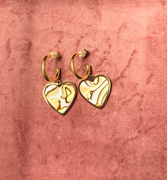 “Mood Swings” oorbellen – goudkleurige hoops met een swirl van goud, witte en bruine marmeren hartvormige bedel, gepresenteerd op een roze fluwelen achtergrond