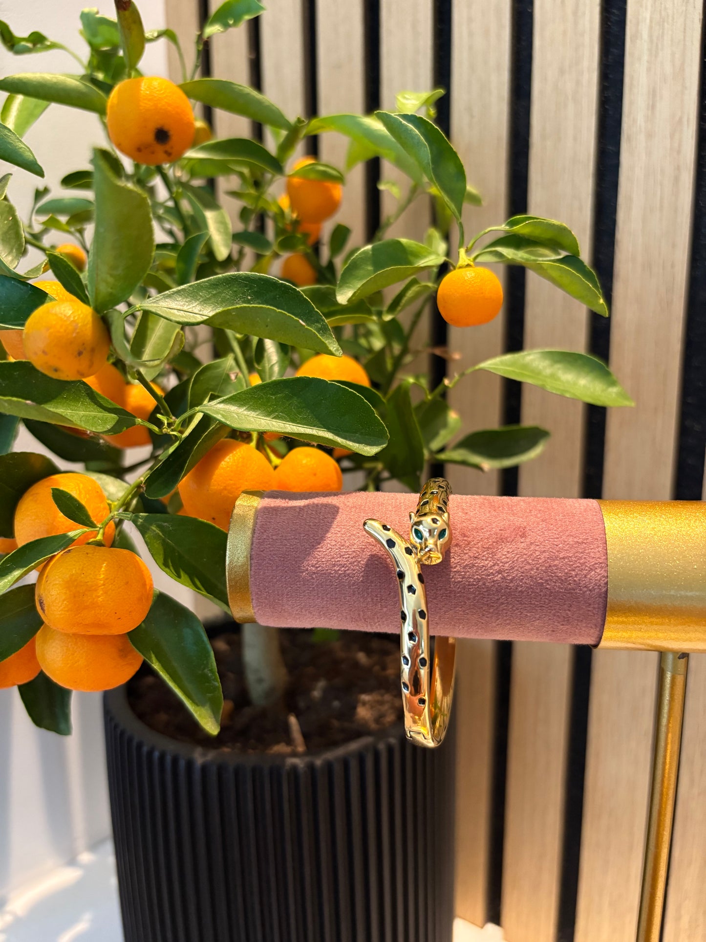 Gouden armband “Queen of the Jungle” met panterprint details, gepresenteerd op een roze displaystandaard