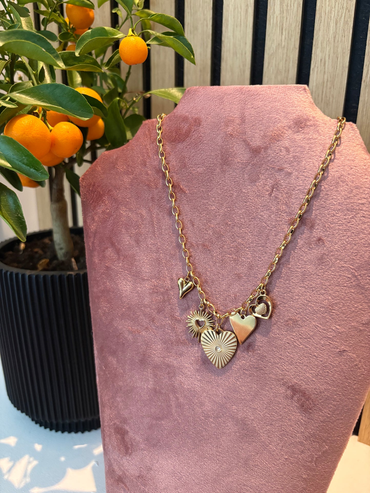 Golden Drama ketting – chunky goudkleurige schakelketting met meerdere hartvormige bedels en zonpatroon hanger, opvallend statement sieraad voor dames.