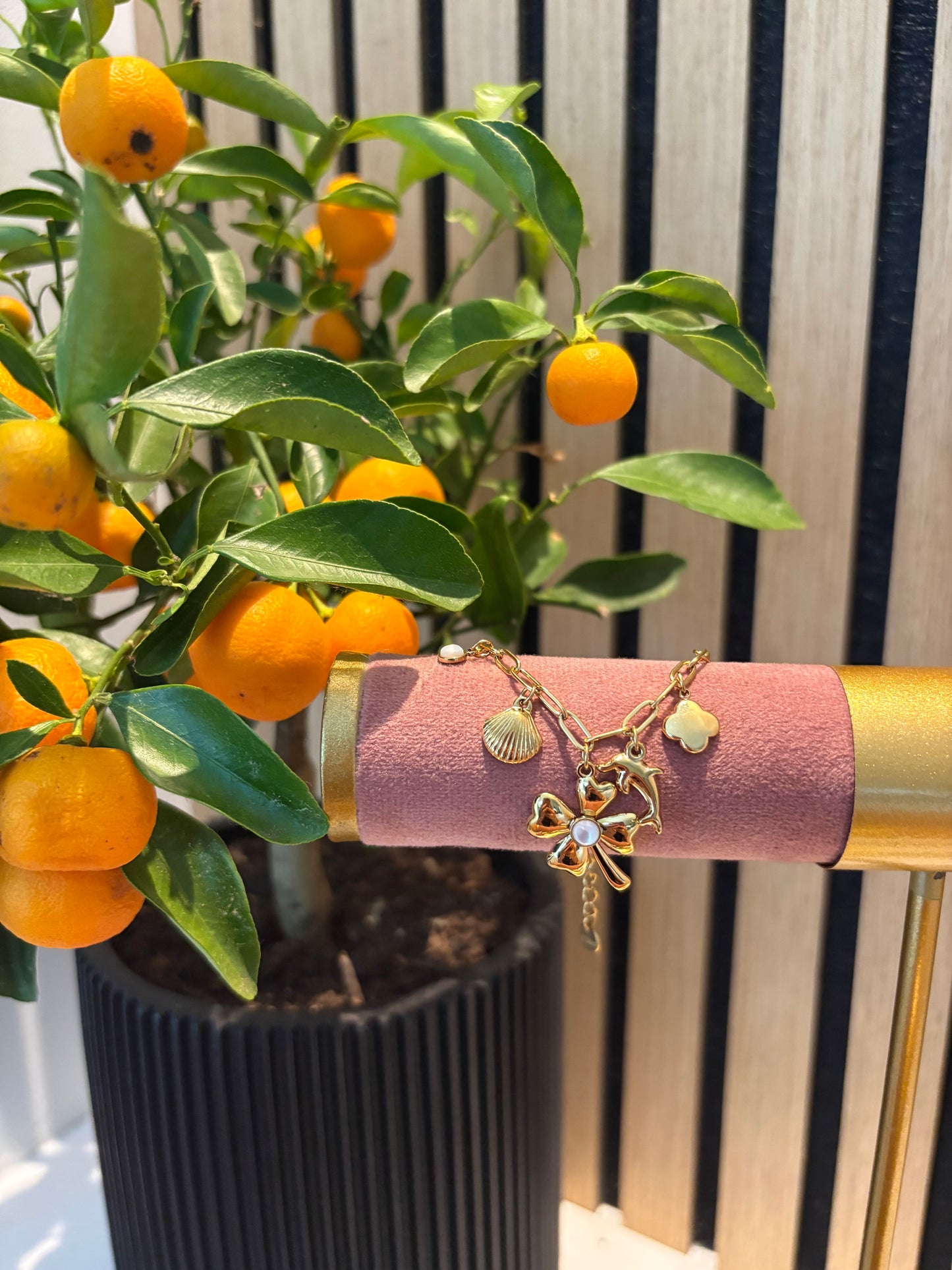 Goudkleurige bedelarmband met klavertjevier en bedeltjes, gepresenteerd op roze fluweel houder.