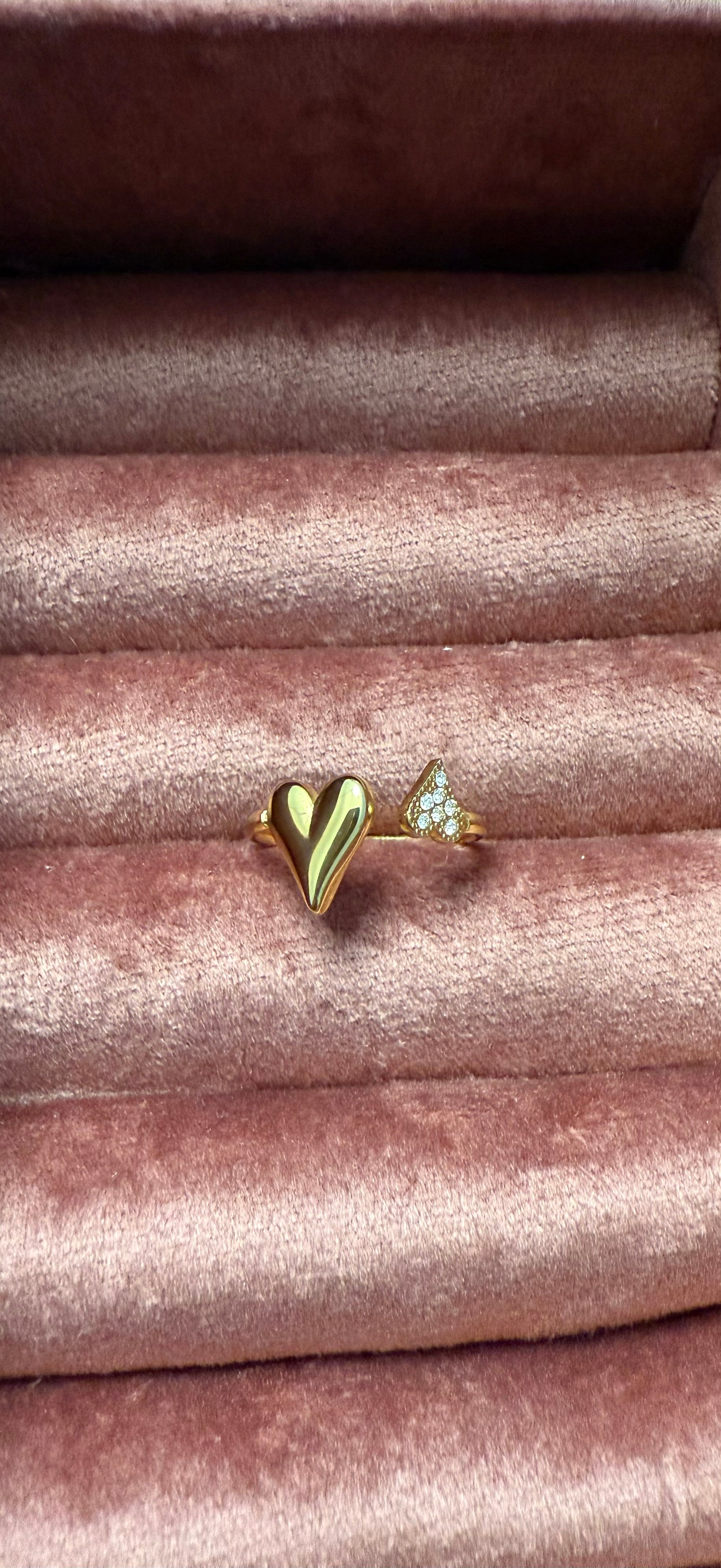 Goudkleurige open stainless steel ring met een glanzend hartje en subtiele zirkonia steentjes, gepresenteerd op roze fluweel