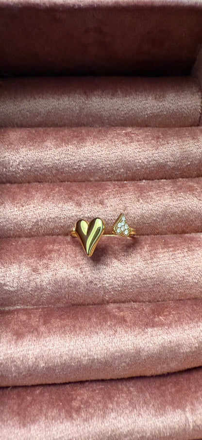 Goudkleurige open stainless steel ring met een glanzend hartje en subtiele zirkonia steentjes, gepresenteerd op roze fluweel