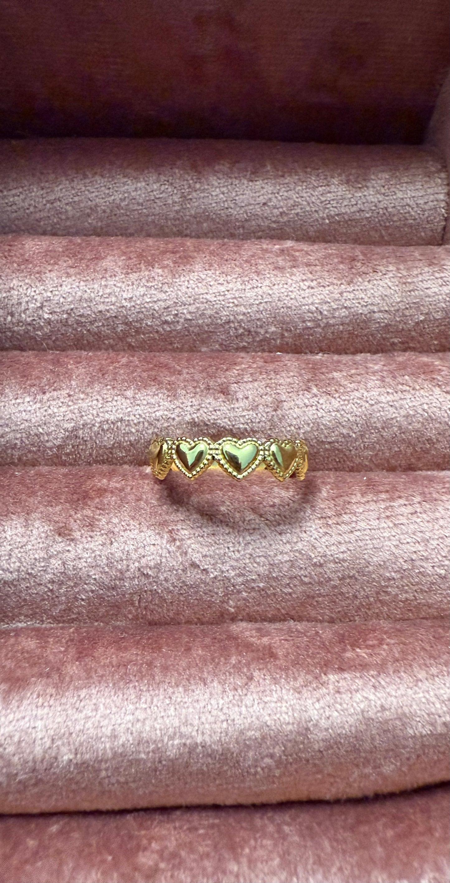 Goudkleurige stainless steel ring met geschakelde hartvormen, gepresenteerd op een roze fluwelen sieradenhouder