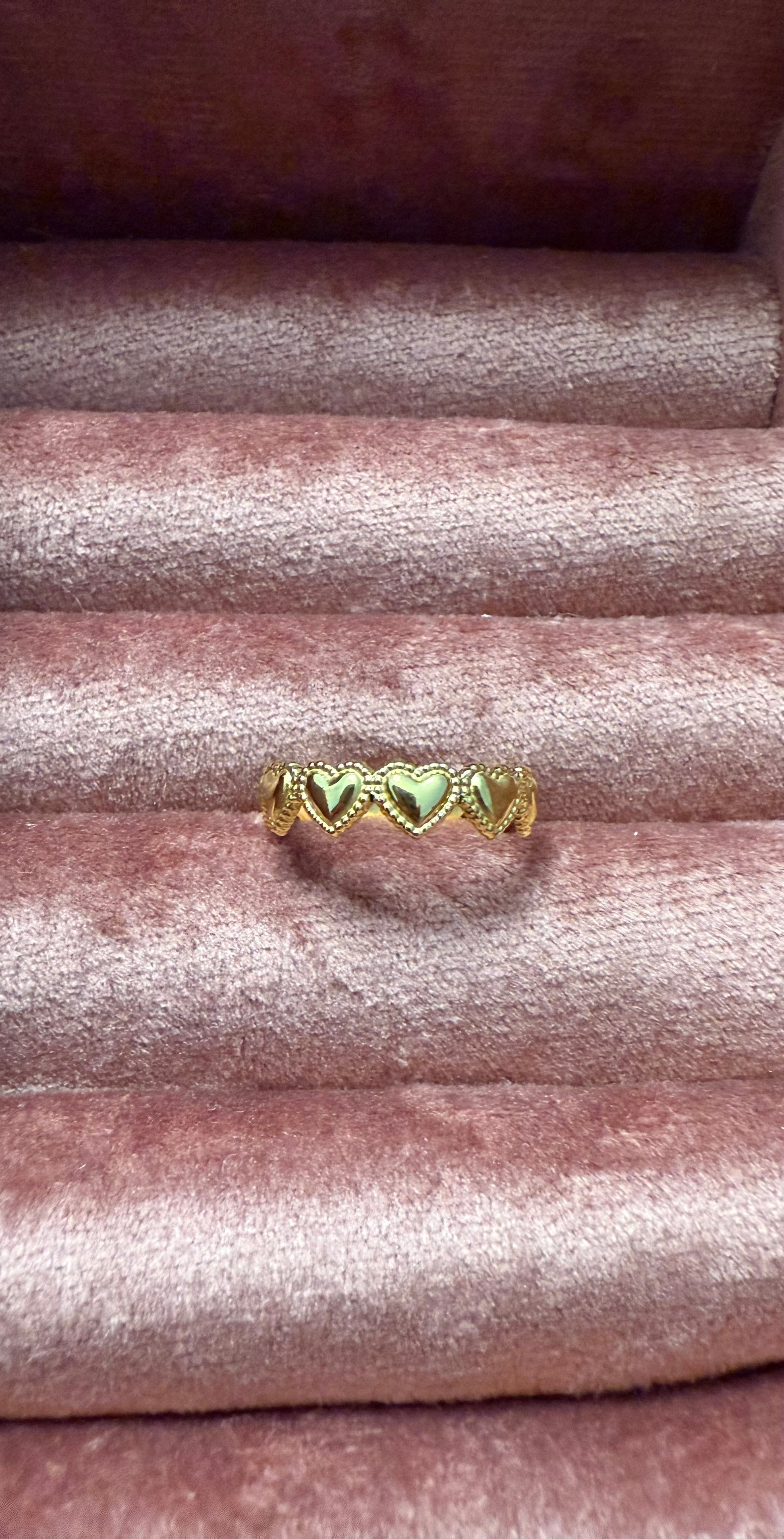 Goudkleurige stainless steel ring met geschakelde hartvormen, gepresenteerd op een roze fluwelen sieradenhouder