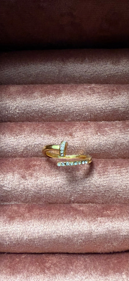 Goudkleurige stainless steel ring met spiraalvorm en zilveren strasssteentjes, gepresenteerd op roze fluwelen sieradendisplay